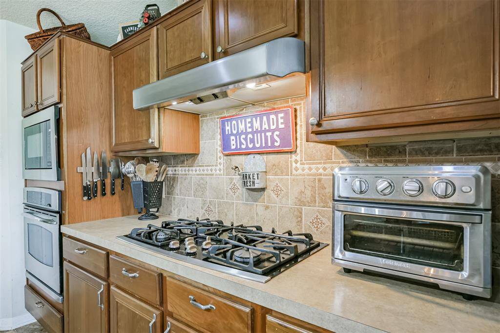 This kitchen features warm wood cabinetry, stainless steel appliances, a gas cooktop, and a decorative tile backsplash.