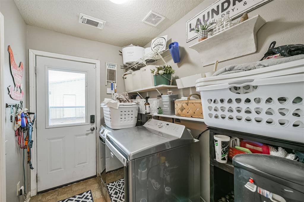 This is a practical laundry room featuring a washer and dryer, ample shelving for storage, and access to the outdoors through a door with a window, allowing natural light to enter the space.