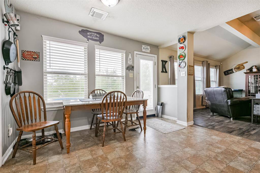 This is a cozy, well-lit dining area. The space features tile flooring, two windows with blinds, and is adjacent to a living area.