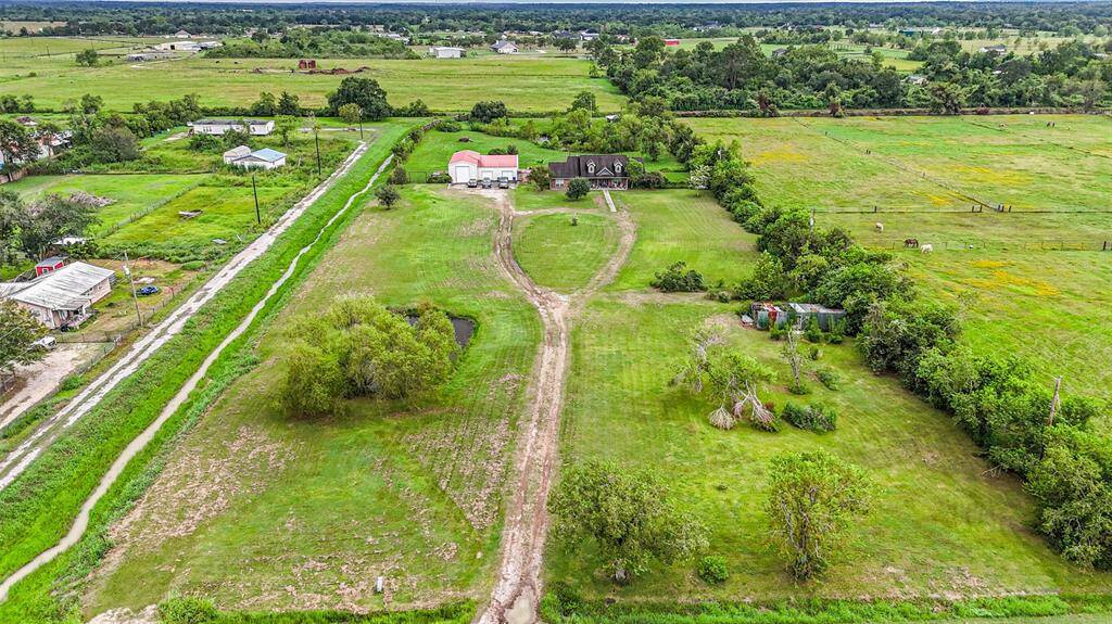 This aerial photo shows a spacious rural property with green fields, a long driveway, and multiple buildings, including a large shop and a cozy house with surrounding trees. The land is well-suited for agriculture or equestrian purposes, offering a serene country lifestyle.