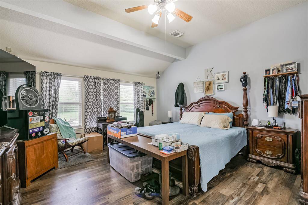 This is a spacious bedroom featuring hardwood floors, a ceiling fan, and multiple windows with patterned curtains.