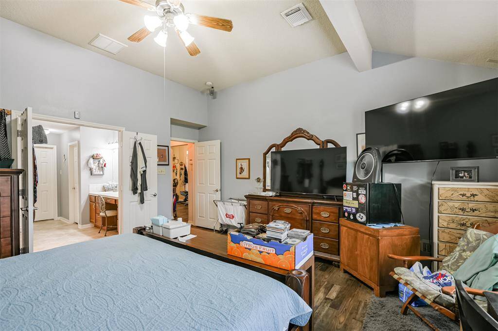 This is a spacious bedroom featuring a high vaulted ceiling with a ceiling fan, multiple doors suggesting an en suite and closet access, and ample space for large furniture and a television setup.