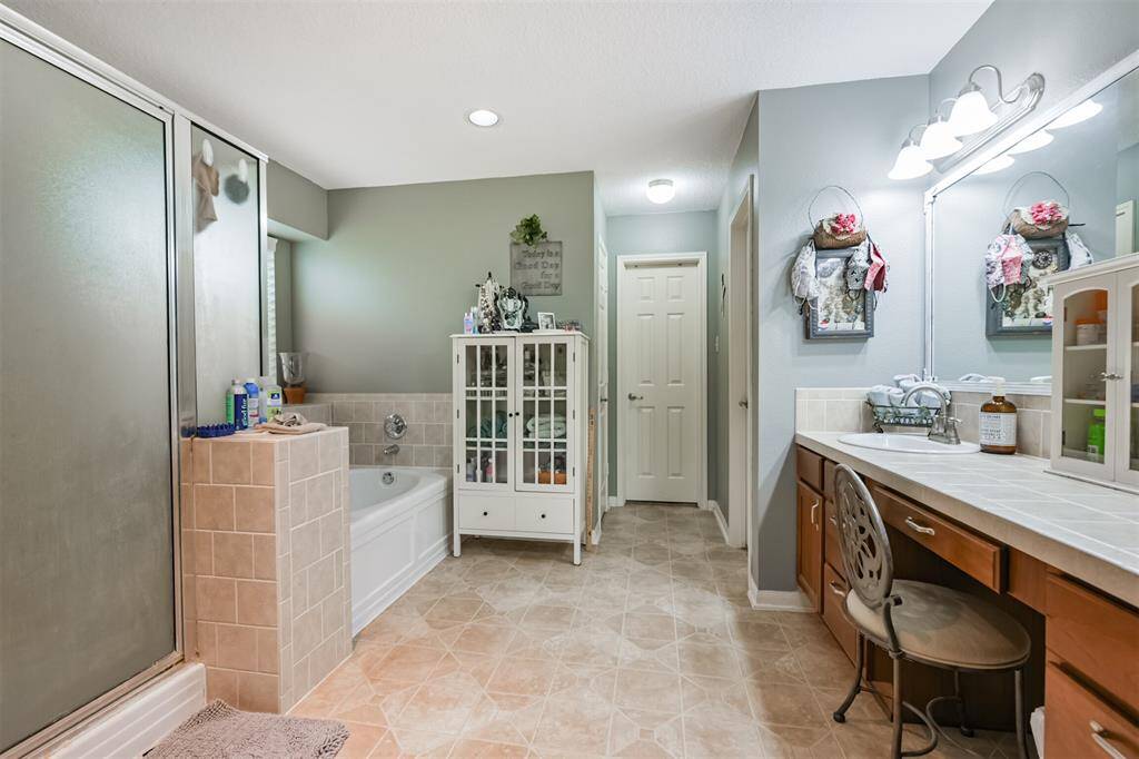 This is a spacious bathroom featuring a large vanity with ample counter space, dual sinks, a frosted glass shower, a separate tub, tiled flooring, and a cabinet for storage. The room is finished with a soothing color palette.