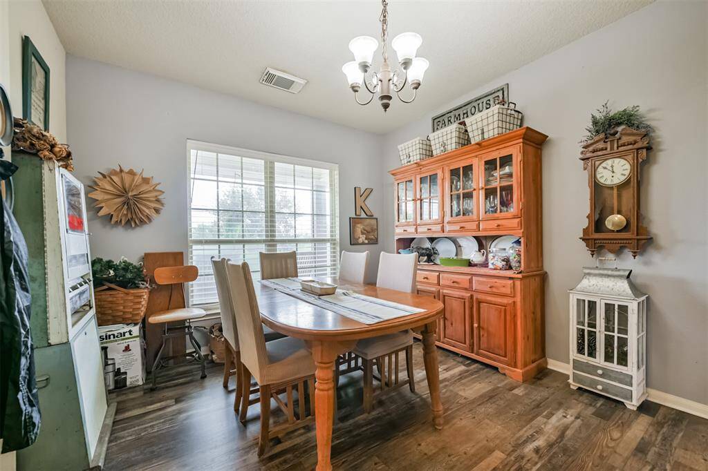 This is a cozy dining area featuring a wooden table with matching chairs, a large window for natural light, and a charming farmhouse-style decor. The room has wood flooring and a simple, inviting ambiance.