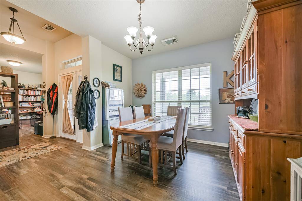 This is an inviting dining area with natural light, featuring wood flooring, a traditional wooden dining set, and a large hutch for storage. The room opens to additional living spaces, creating an open and airy feel.