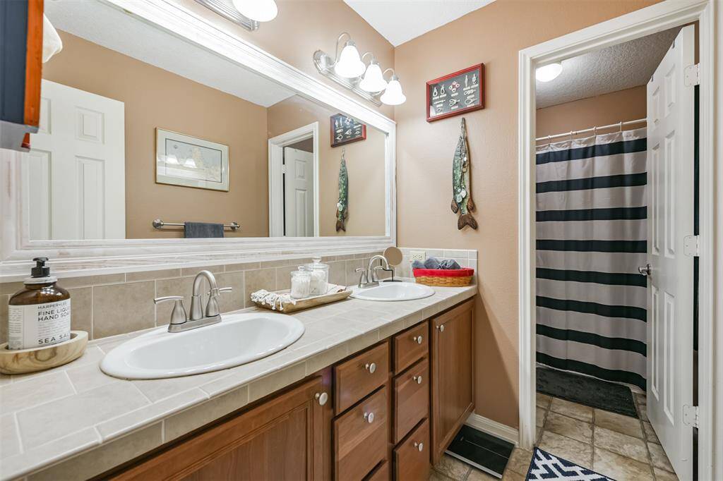This is a well-maintained bathroom featuring a large vanity with dual sinks, a wide mirror with overhead lighting, and a separate shower area with a striped curtain. The room has a warm color scheme and decorative touches that create a cozy atmosphere.