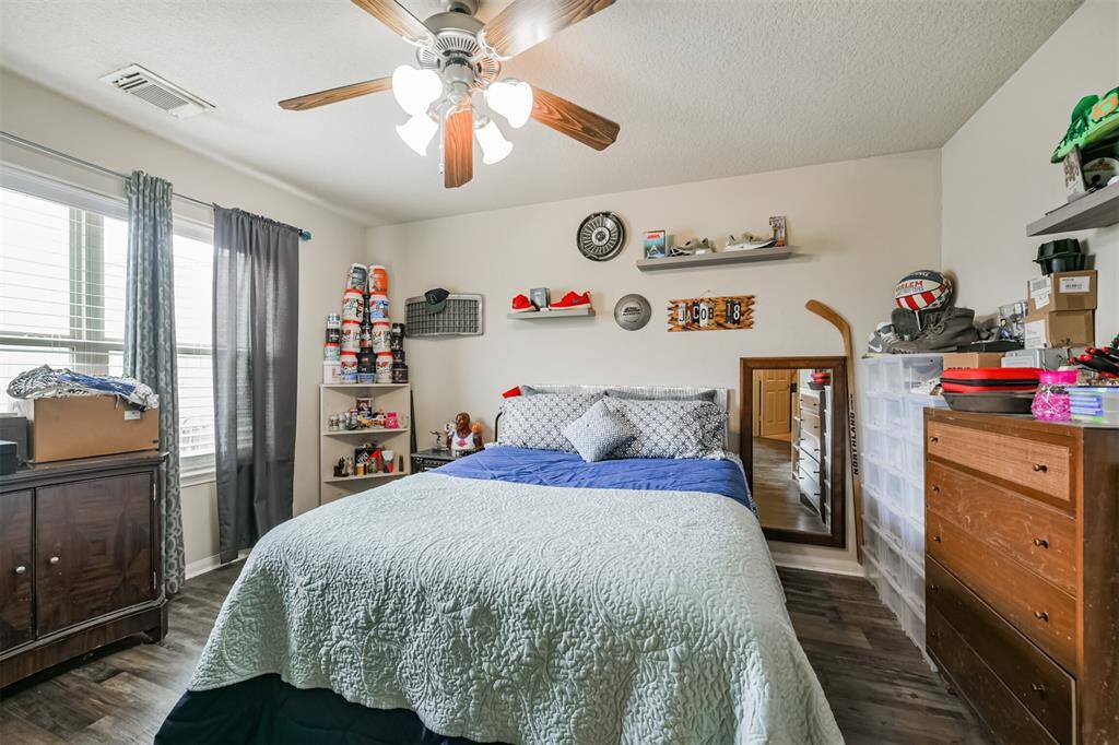 This is a well-lit, cozy bedroom featuring a ceiling fan, hardwood floors, and a window.