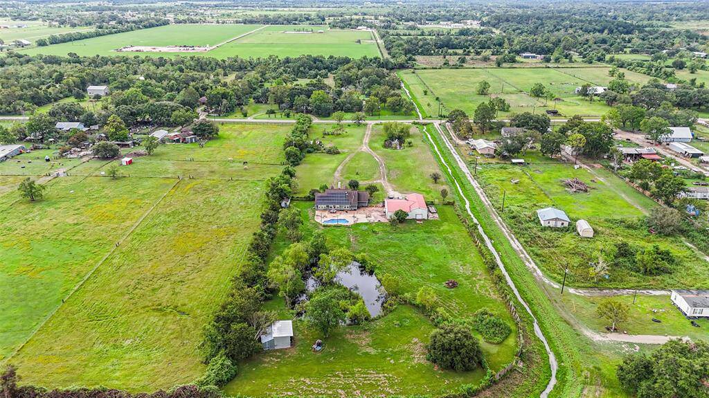 This aerial photo showcases a rural property with an expansive green lawn, a large pond, and a spacious home with a pool. The property is surrounded by open fields and scattered houses, offering a sense of seclusion and open space.
