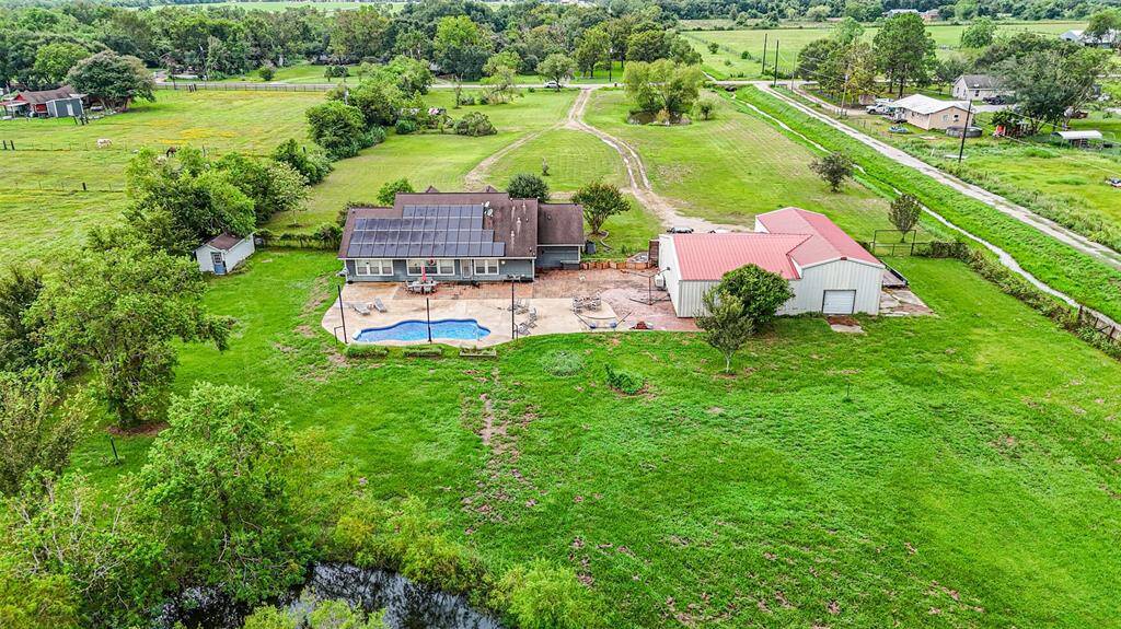 Spacious property featuring a single-family home with solar panels, a private swimming pool, a large detached garage/shop, and expansive green lawns, all set in a serene rural setting with open fields and scattered trees.