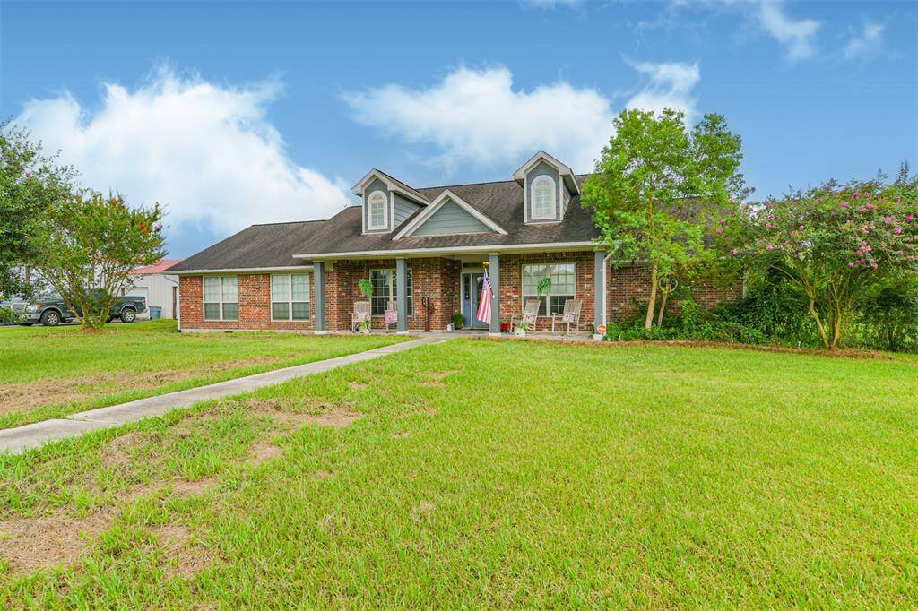 This is a single-story brick home with a well-manicured lawn and mature landscaping. It features a pitched roof with dormer windows and a cozy front porch.