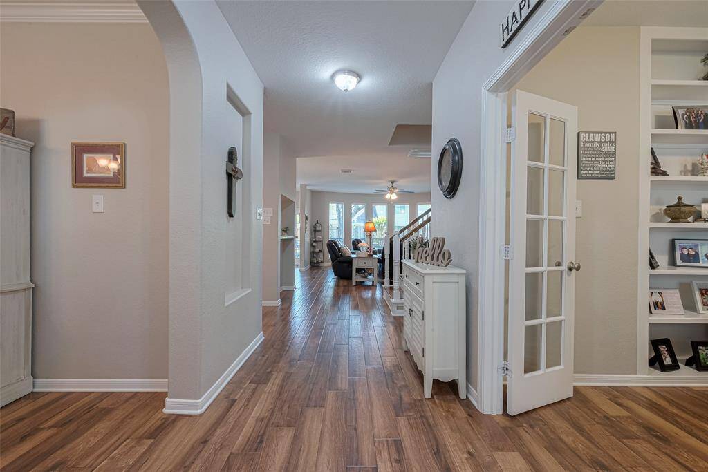 The entryway highlights the home’s neutral palette & wood-look tile flooring. To the right beyond the French doors is a dedicated office with built-in shelving and a formal dining room is on the left.
