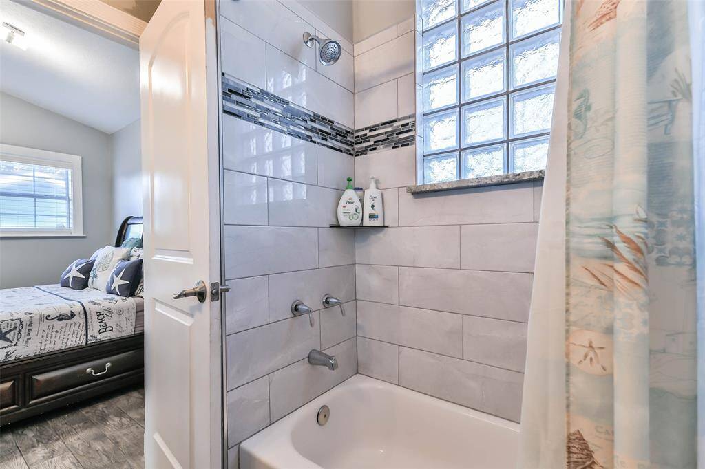 A tub and shower featuring ceramic tile walls and a glass block window,