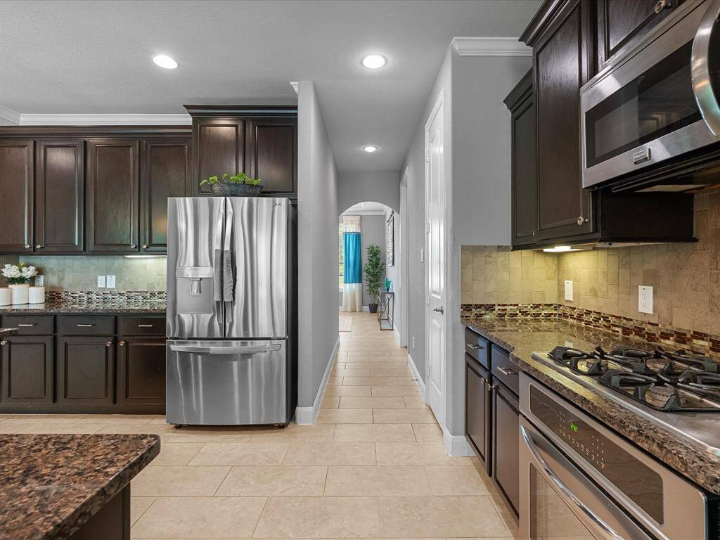 This modern kitchen features dark wood cabinetry, granite countertops, and stainless steel appliances, including a gas stove and microwave. The backsplash combines neutral tiles with a decorative border. The space is well-lit and opens into a cozy dining area.