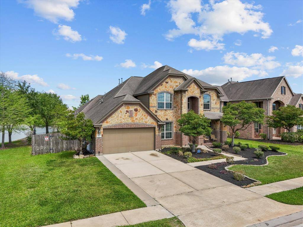 This beautiful two-story brick home features a well-maintained front yard and a spacious driveway. It is located in a serene neighborhood with a picturesque lake view, complete with a fountain and lush greenery.
