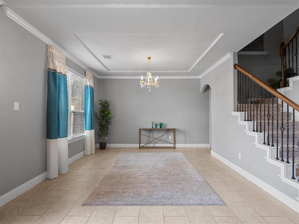 This spacious and elegant entryway features neutral tile flooring, a stylish staircase with wrought-iron railings, and a beautiful chandelier. Arched doorways lead to an open living area and dining space, creating a welcoming atmosphere.