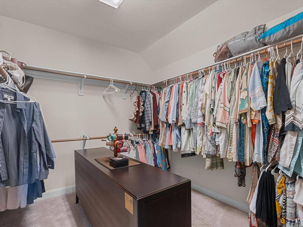 Spacious walk-in closet with ample hanging space and a central island, perfect for organizing clothes and accessories located in primary bedroom.