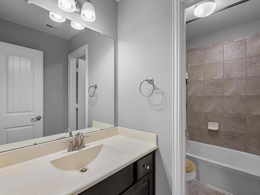 This bathroom features a modern vanity with a sleek sink, large mirror, and overhead lighting. The room includes a tiled bathtub and shower combination, complemented by neutral wall colors for a clean and fresh look.