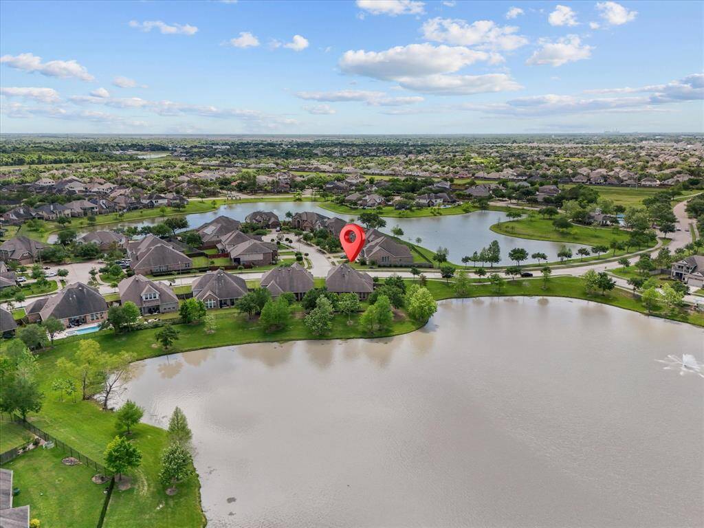 This aerial photo showcases a serene residential neighborhood with spacious homes surrounded by lush greenery and multiple lakes. The highlighted property is located on water front property offering picturesque views and a tranquil atmosphere.