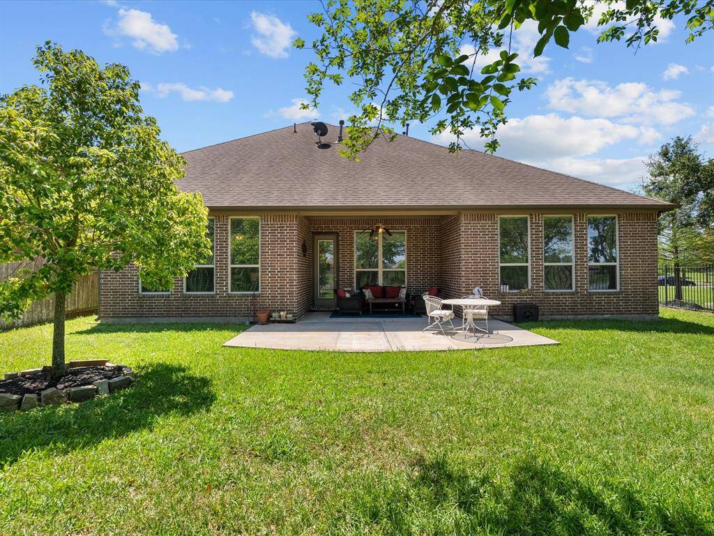This photo showcases a cozy backyard with a well-maintained lawn and a brick house featuring large windows. There's a  patio area with seating, perfect for outdoor relaxation or entertaining. Lush greenery surrounds the space, adding privacy and charm.