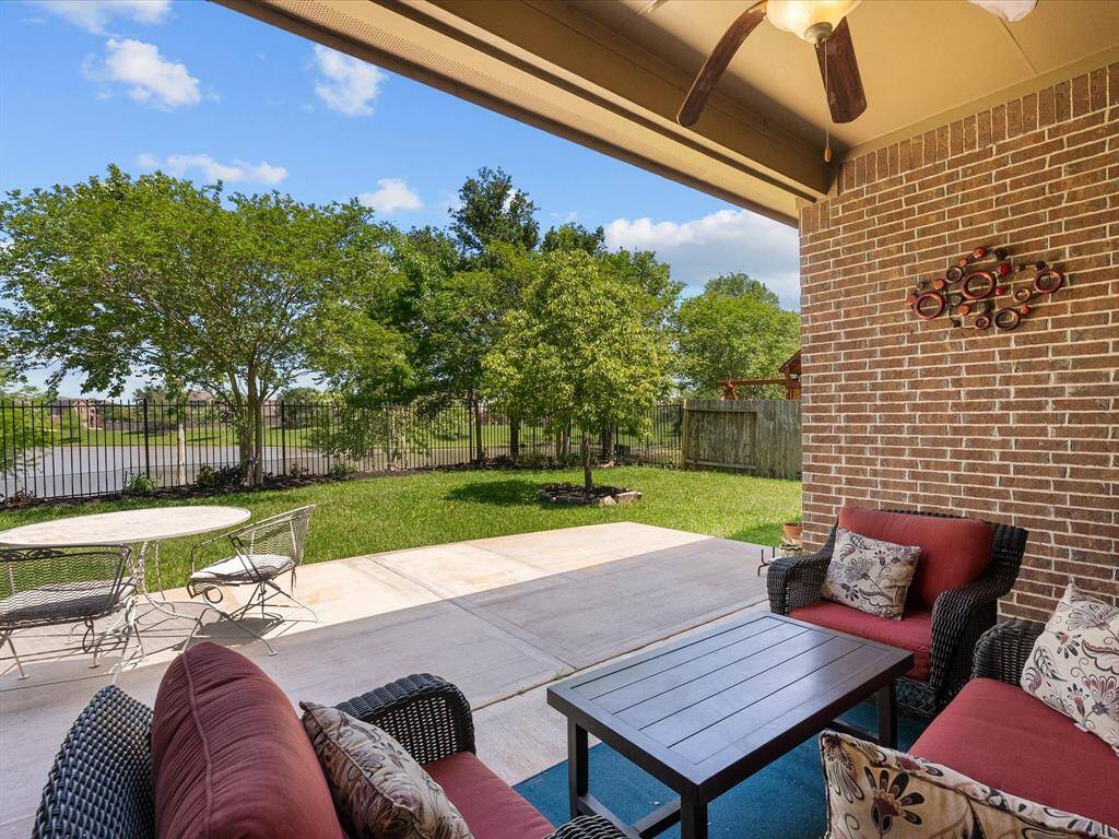 This photo showcases a charming patio with comfortable seating and a ceiling fan, overlooking a lush, fenced backyard. Ideal for outdoor relaxation and entertaining, it offers a serene view of greenery and open skies.