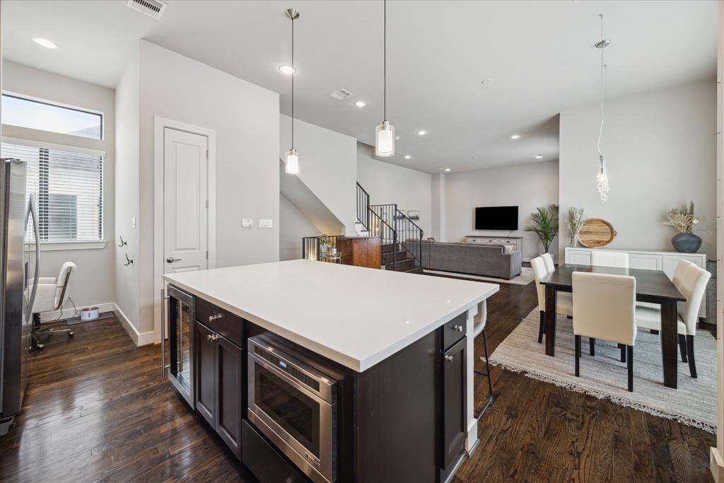 The oversized quartz island does triple duty, adding storage, housing the wine refrigerator and microwave and accommodating seating for four under modern pendant lighting.