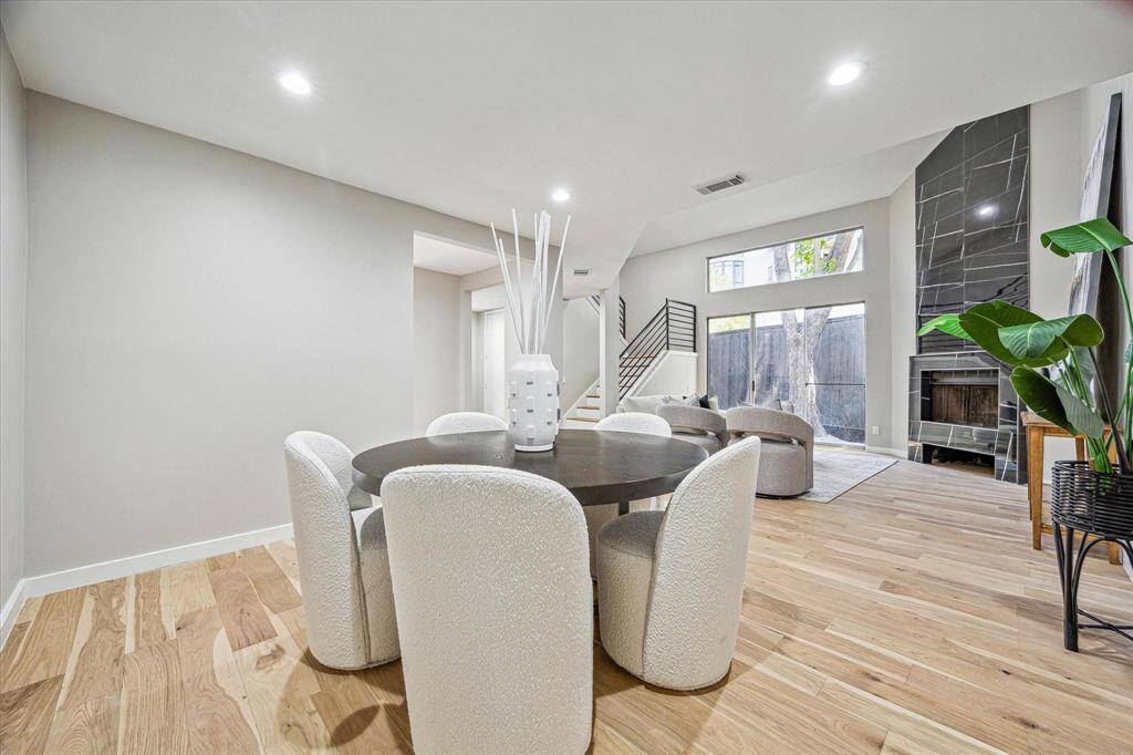 This impressive two-story living room features gorgeous White Oak engineered flooring, fresh neutral paint, and a dramatic floor-to-ceiling marble look fireplace. Sleek metal railings line the stairs and balcony, while oversized glass doors open to a private outdoor space, creating an open and airy modern retreat.