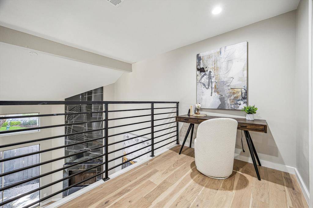 From the stairs, take in the view of the open, airy two-story living room below. Updated metal railings line the loft and staircase, perfectly complementing the White Oak engineered hardwood floors, fresh neutral paint, and clean architectural lines creating a visually striking space.