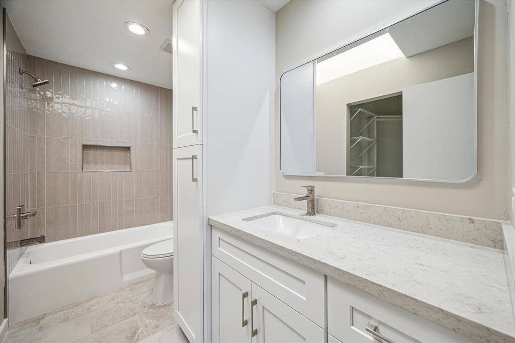 The luxurious guest accommodations continue into this beautifully updated private ensuite, featuring a Quartz-topped single-sink vanity with modern fixtures, linen storage, a sleek mirror, and a fully tiled tub/shower enclosure with custom nook.