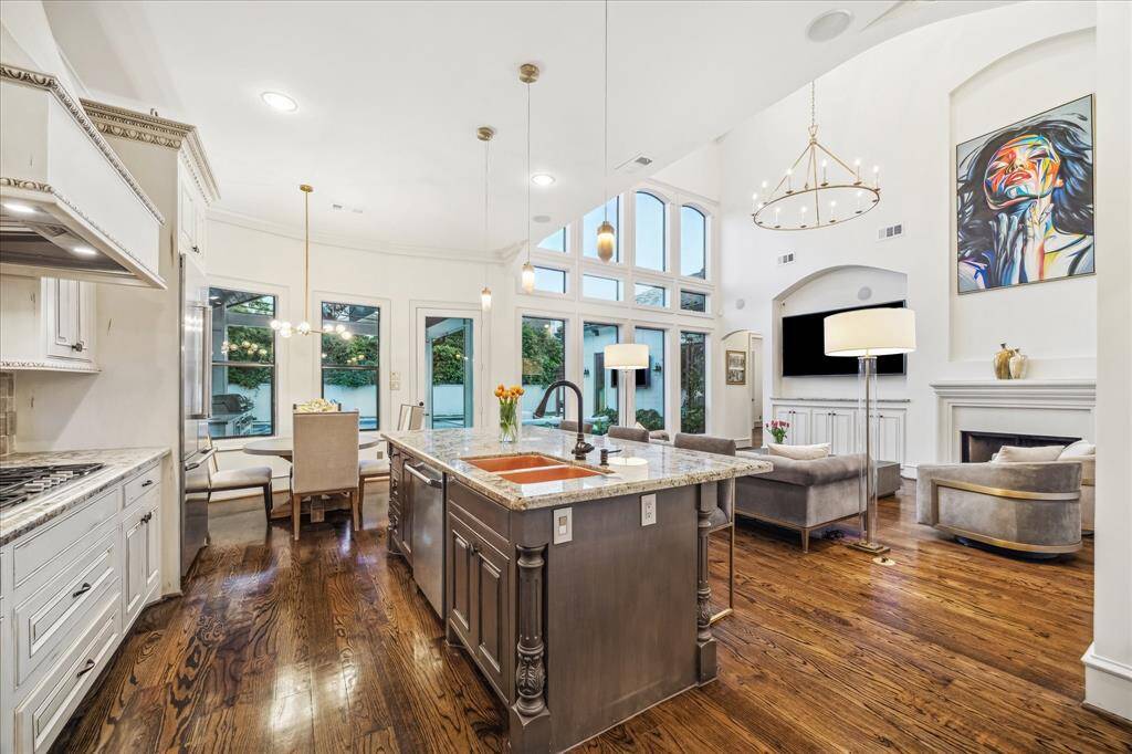 This spacious open-concept kitchen and living area features high ceilings, large windows, and elegant finishes. The kitchen boasts a central island with a sink and modern appliances, while the living area offers a cozy fireplace and ample seating. Contemporary lighting and artwork enhance the stylish ambiance.