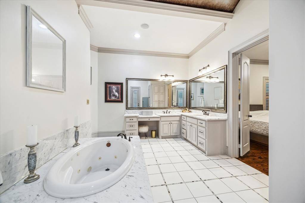 This spacious master bathroom features a luxurious jetted tub, dual sinks with ample counter space, elegant marble countertops, and large mirrors. The neutral tones and well-lit space add to its serene atmosphere, while the adjacent bedroom access enhances convenience.