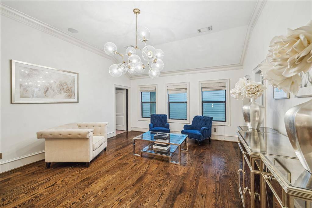 This elegant living room/ game room on the second floor features rich hardwood floors, a modern chandelier, and ample natural light from three large windows.