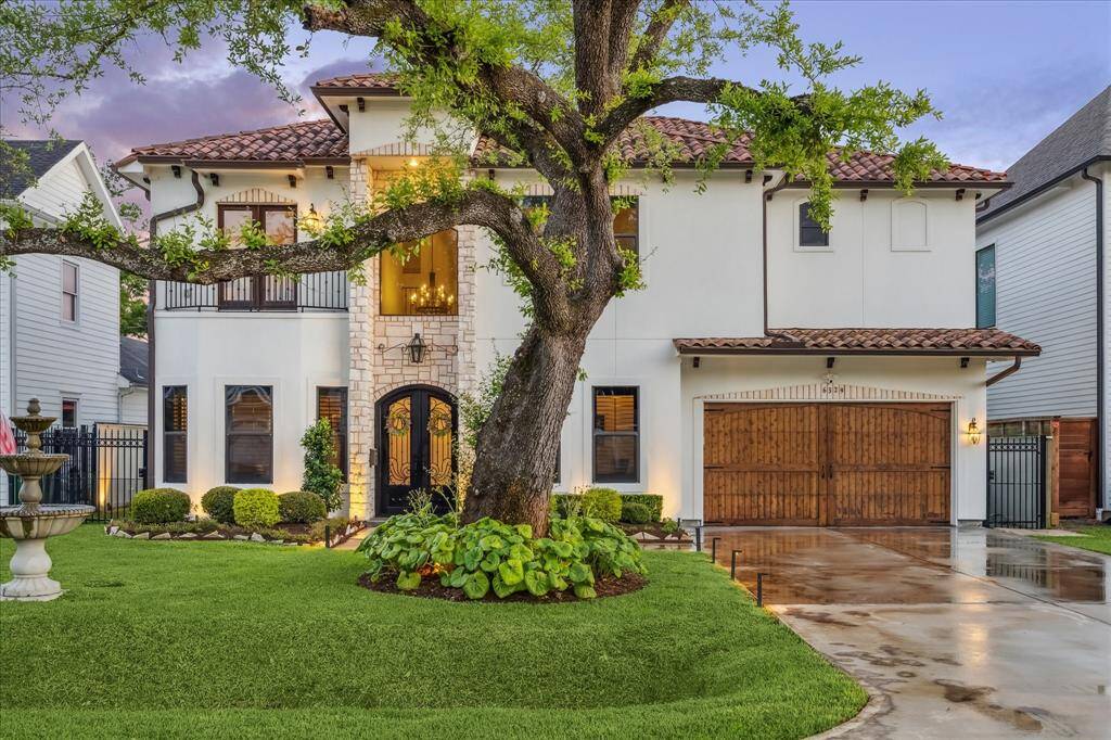 This elegant two-story home features a Mediterranean-style facade with a beautiful stone entrance and arched wooden doors. The lush front yard includes a large tree and a decorative fountain, while the driveway leads to a spacious two-car garage. Perfect for those seeking charm and sophistication.