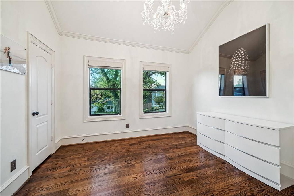 Bright room with hardwood floors, two large windows, and a modern white dresser. Features a vaulted ceiling with an elegant chandelier. Ideal for a bedroom or home office.