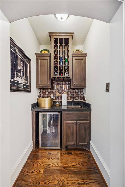 This cozy bar nook on the second floor features elegant dark wood cabinetry, a wine rack, and a compact fridge. It includes a sink and a stylish tile backsplash, perfect for entertaining in a small space.