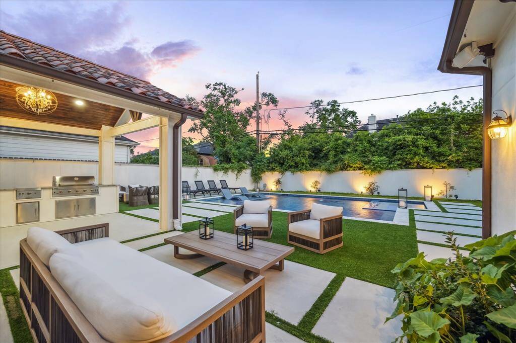 This elegant backyard features a modern pool, a cozy seating area, a covered patio with a covered outdoor kitchen, built-in grill, wine cooler and stylish landscaping, perfect for outdoor entertaining.