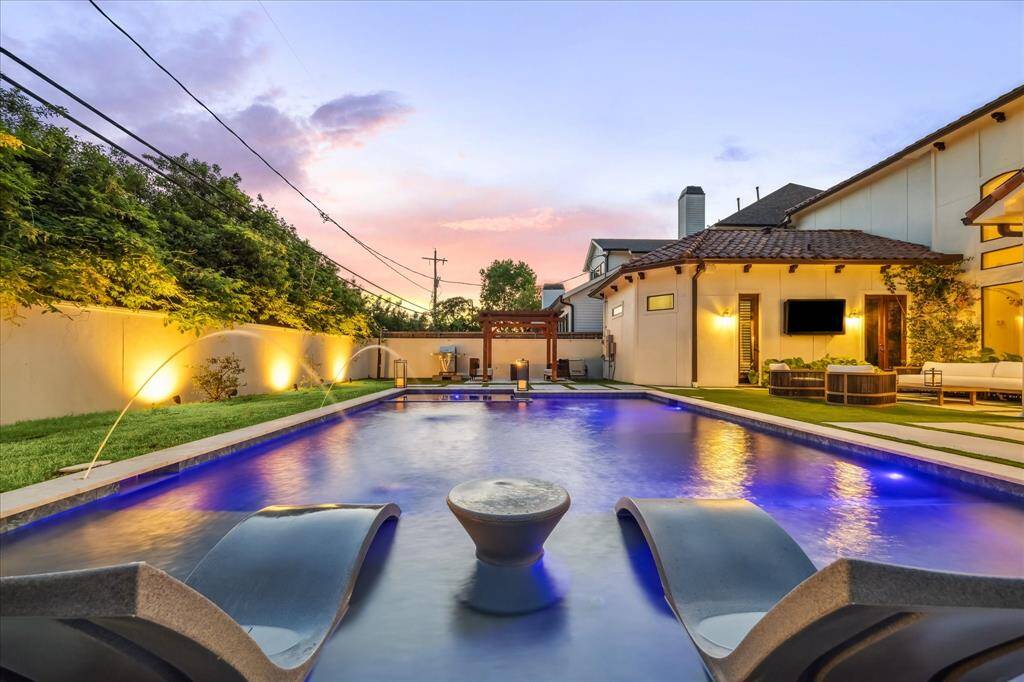 This photo showcases a luxurious backyard with a modern pool, elegant lighting, and comfortable lounge chairs. The surrounding area features well-maintained landscaping and a stylish outdoor living space, perfect for relaxation and entertainment.