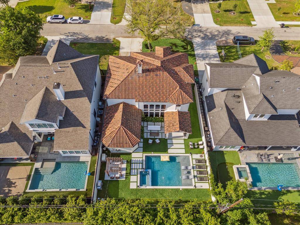 This aerial view showcases a luxurious home featuring a spacious backyard with a large pool and outdoor seating area. The house has a distinctive red-tiled roof and is nestled between two neighboring homes, each with their own pools. Ideal for those seeking a stylish property with ample outdoor entertainment space.