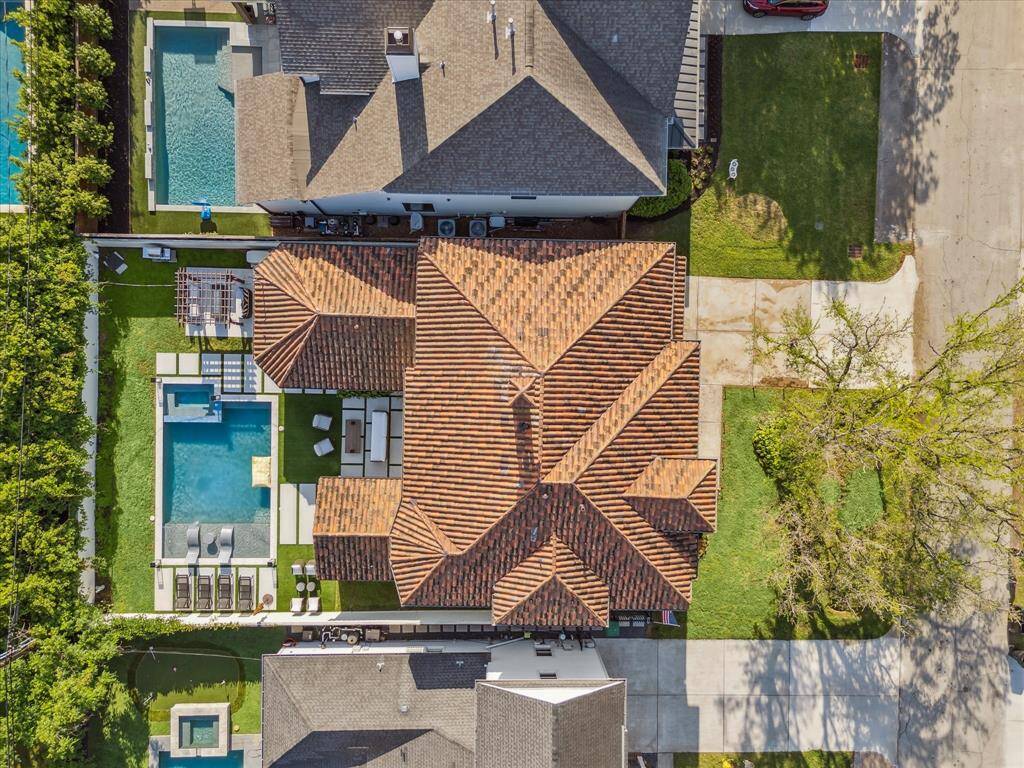 This aerial view showcases a spacious home with a distinctive tiled roof. It features a large backyard with a swimming pool, ample patio seating, and landscaped greenery. The property is situated in a suburban neighborhood with well-maintained surroundings.