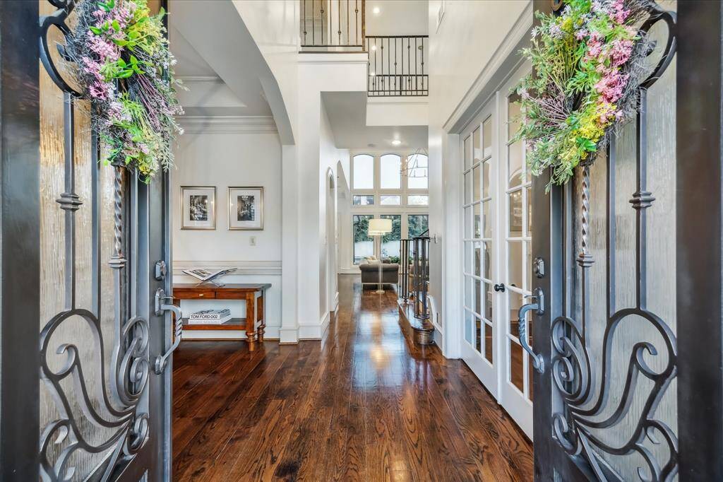This entrance features elegant double doors adorned with floral wreaths, leading into a bright, open foyer with high ceilings and rich hardwood floors. The space offers a glimpse into a stylish living area with large windows, filling the home with natural light.