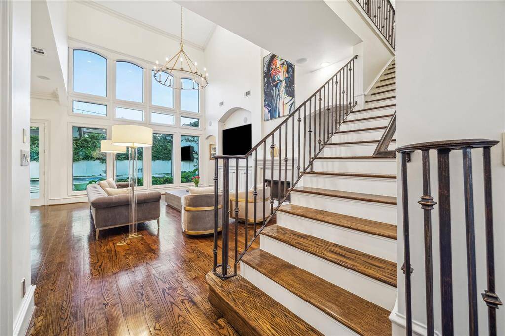 This elegant living space features high ceilings, large windows for natural light, hardwood floors, and a stylish staircase. The room is spacious and modern, with contemporary furnishings and a chic chandelier. Perfect for comfortable living and entertaining.