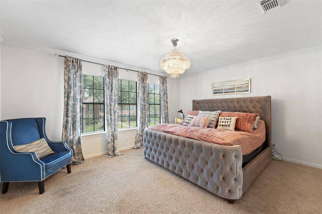Bright and inviting, this secondary bedroom offers soft carpet, elegant window treatments, and a stylish chandelier.