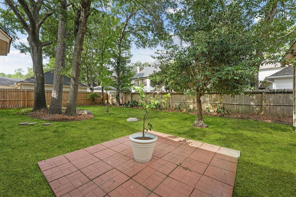 The private backyard offers a peaceful retreat with mature trees, green space, and a cozy brick patio—ideal for outdoor living.