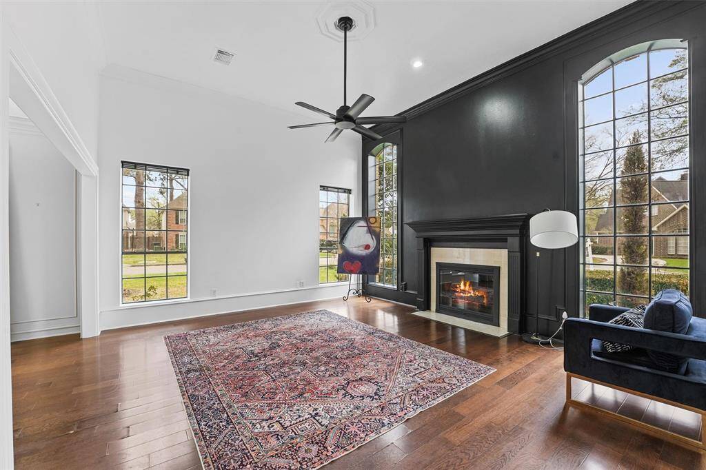 This stunning living room features a dramatic black accent wall, elegant fireplace, expansive windows, and vaulted ceilings that fill the space with natural light.