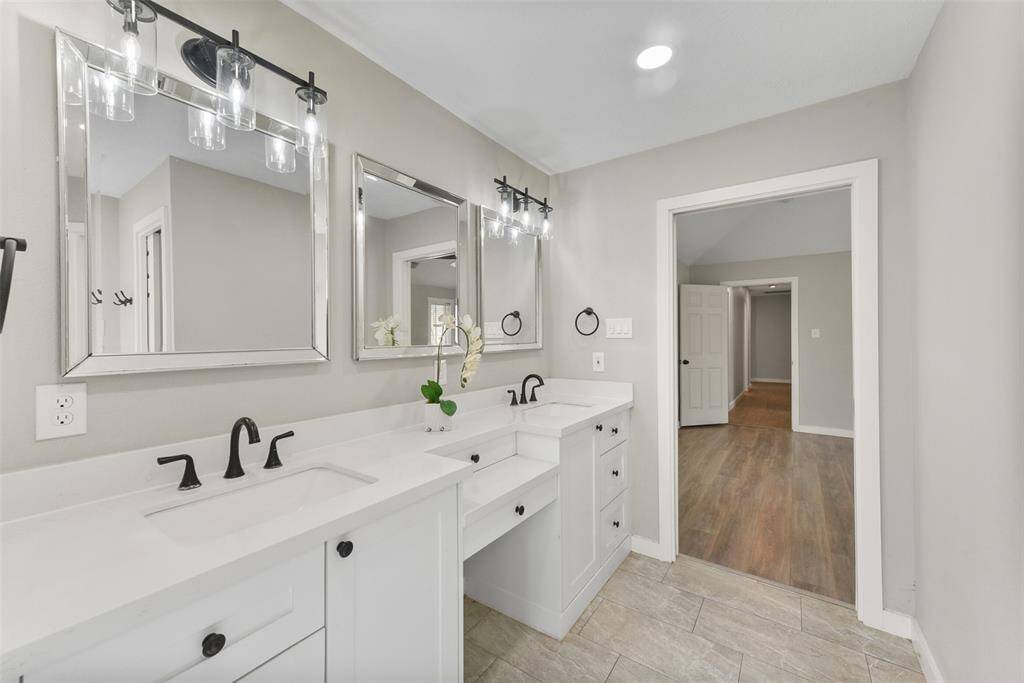 The master bathroom underwent a full remodel in 2021 that included a new seated vanity with a dual-tier lap drawer, ample storage, quartz countertops, dual rectangular basin sinks, updated hardware & lighting, and a trio of beveled frame mirrors.