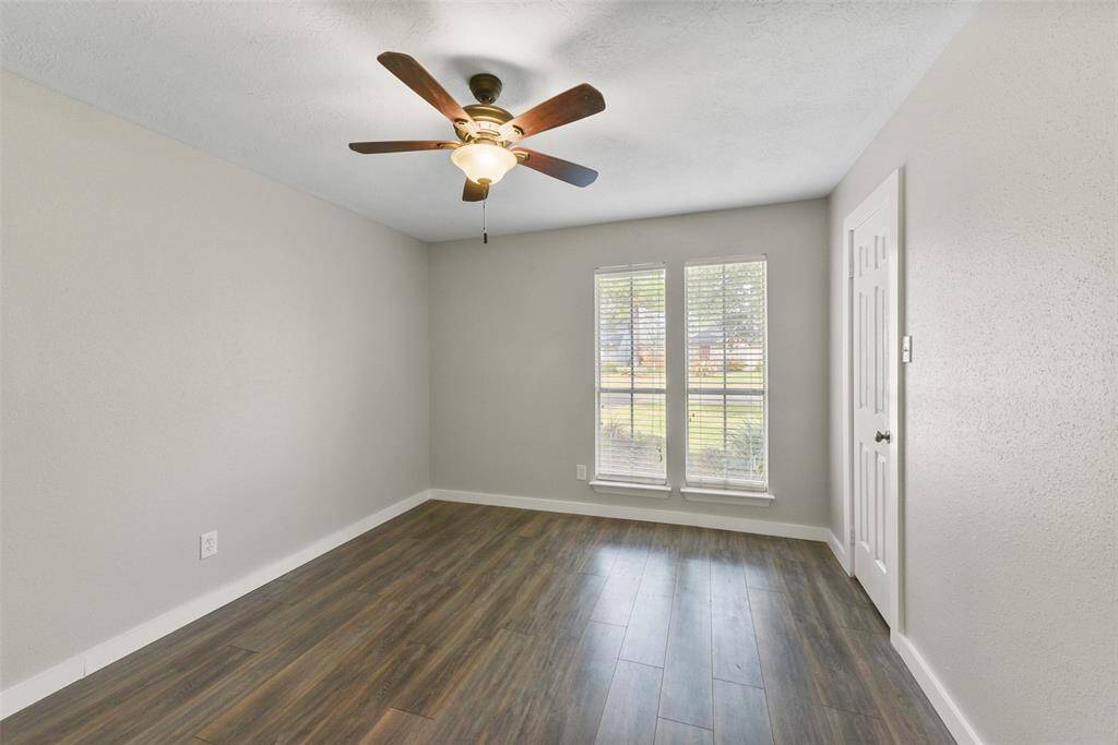 The first of three similarly finished secondary bedrooms features fresh neutral paint, an updated lighted ceiling fan, a walk-in closet with extra shelving, and a pair of front-facing windows with 2-inch blinds and front yard views.