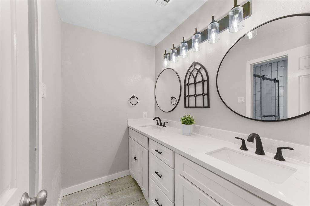 The guest bathroom has also been completely renovated to include a lengthy white vanity with stylish matte black hardware, a quartz countertop, dual rectangular sinks, framed mirrors, designer lighting, and an oversized shower with detailed tilework & a sliding glass door.