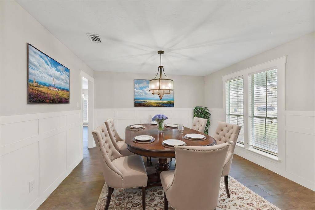 A wide entrance off of the right side of the foyer leads into this inviting formal dining room with stylish block paneling, neutral paint, designer lighting, wood look-tile floors, direct kitchen access, and a pair of cased windows with 2-inch blinds & front yard views.