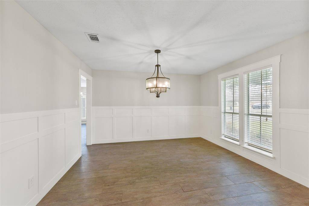 A wide entrance off of the right side of the foyer leads into this inviting formal dining room with stylish block paneling, neutral paint, designer lighting, wood look-tile floors, direct kitchen access, and a pair of cased windows with 2-inch blinds & front yard views.