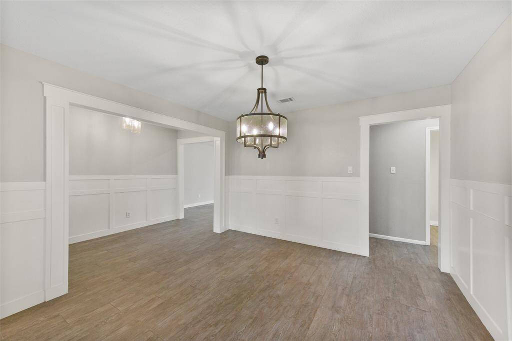 A wide entrance off of the right side of the foyer leads into this inviting formal dining room with stylish block paneling, neutral paint, designer lighting, wood look-tile floors, direct kitchen access, and a pair of cased windows with 2-inch blinds & front yard views.