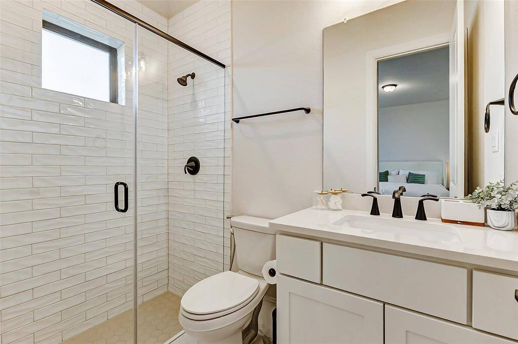 The guest bathroom features a beautifully designed walk-in shower with a stunning subway tile surround and elegant bronze finishes. A stylish vanity with matching bronze hardware and an under-mount sink complete this sophisticated space.